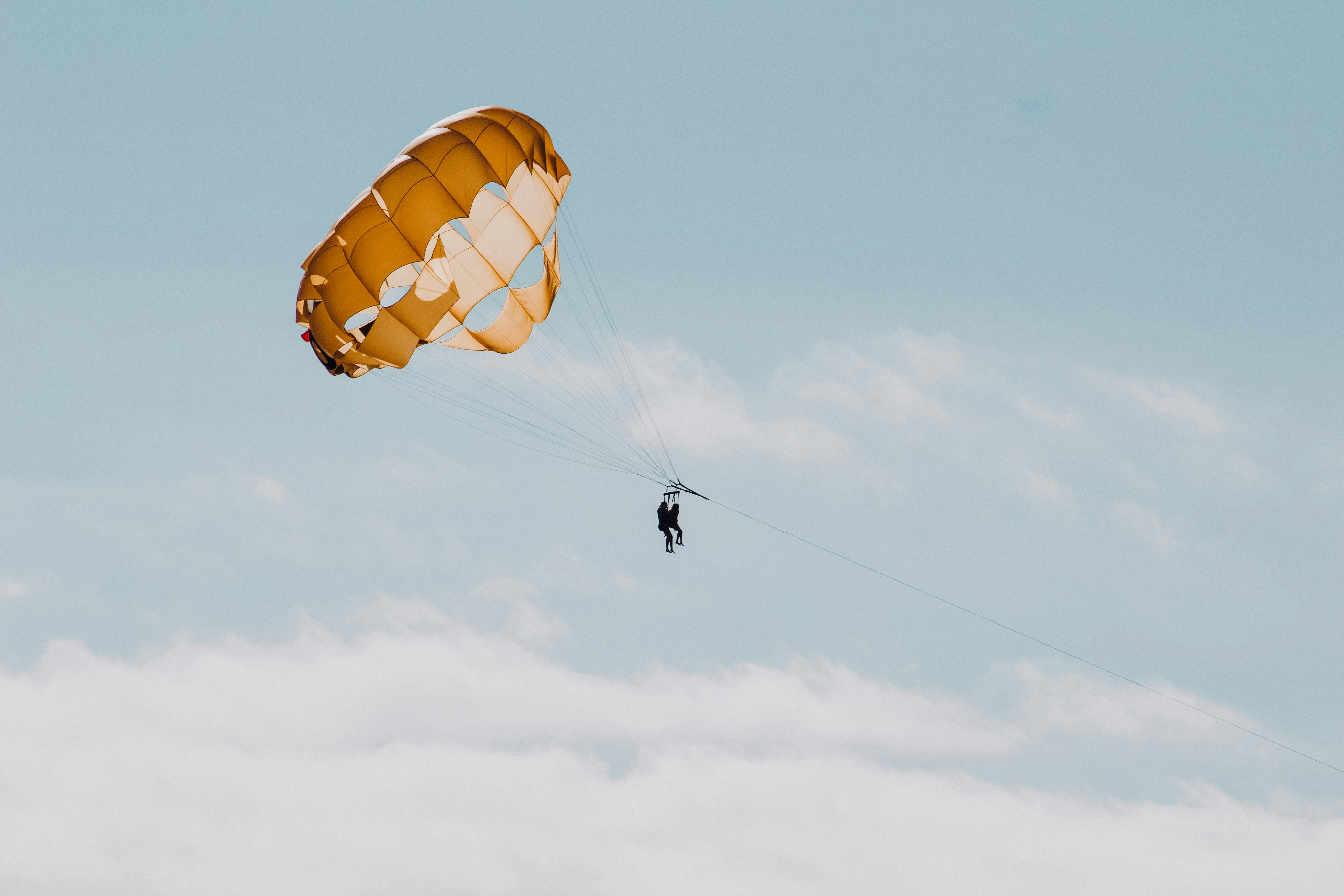 Person parasailing above the clouds under a golden parachute